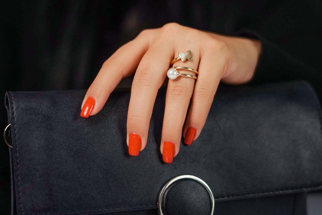 Close-up of a woman's hand with gold rings and red nails on a black leather bag.