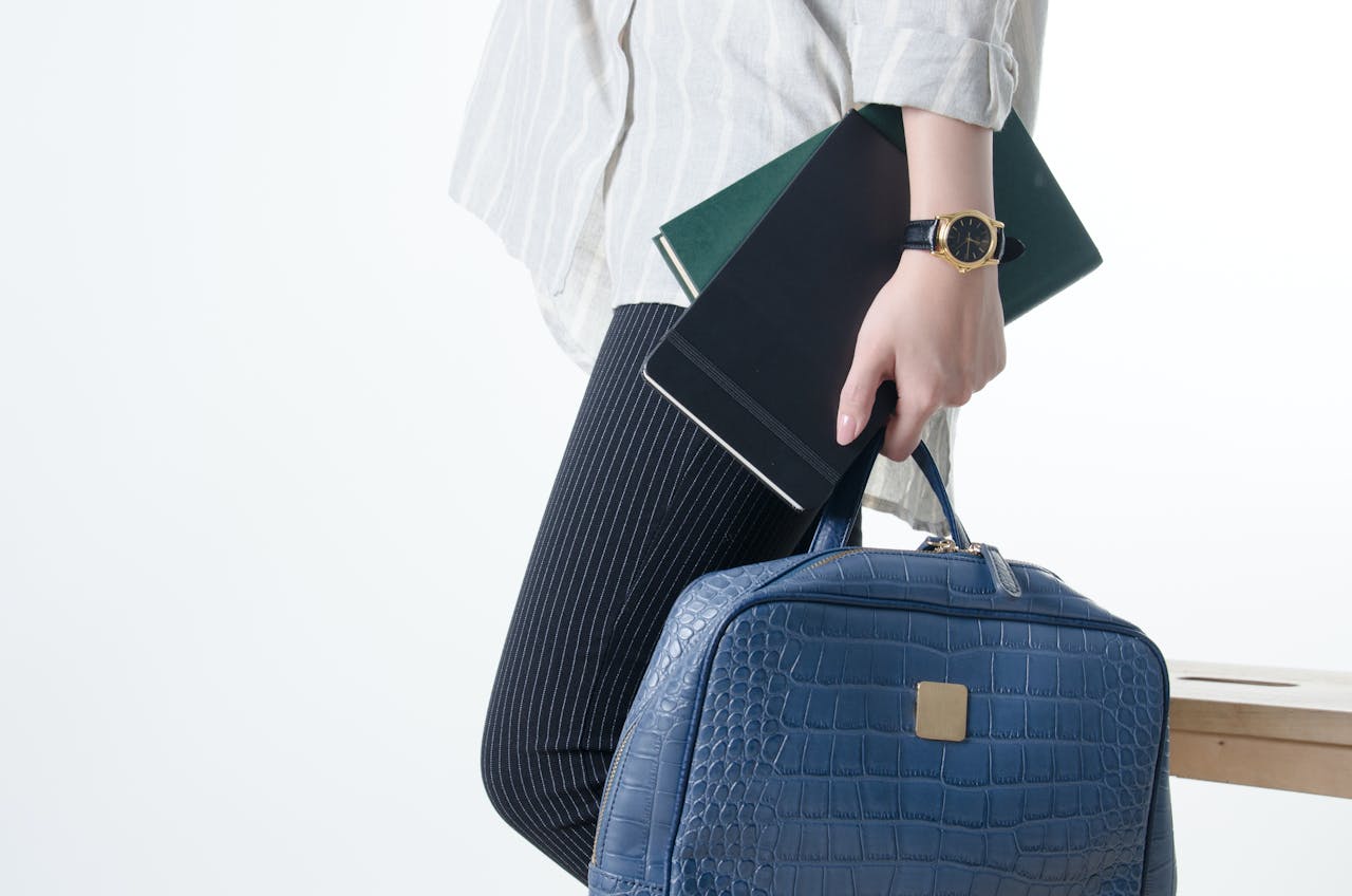Close-up of a stylish individual holding a blue leather bag and notebooks, showcasing modern business fashion.